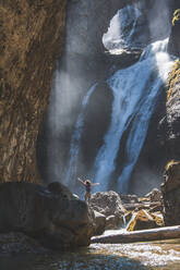 Spanien, Provinz Huesca, Wanderin steht mit erhobenen Armen am Fuße eines plätschernden Wasserfalls - FVSF00210