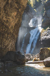 Spanien, Provinz Huesca, Wanderin steht mit erhobenen Armen am Fuße eines plätschernden Wasserfalls - FVSF00211