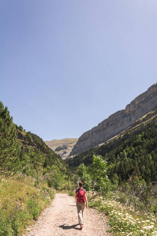 Spain, Province of Huesca, Clear sky over female backpacker hiking along mountain dirt road stock photo