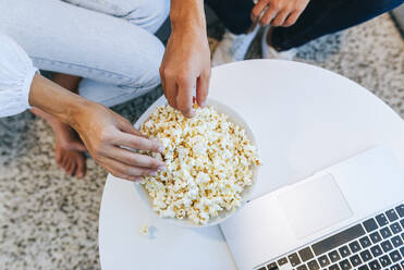Niedriger Ausschnitt eines Paares mit Popcorn am Laptop am Tisch im Haus - KIJF02979