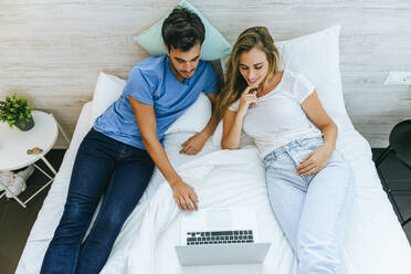 High angle view of couple watching movie on laptop while relaxing on bed at home - KIJF02990