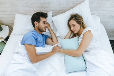 Smiling man looking at partner sleeping on bed at home - KIJF02992