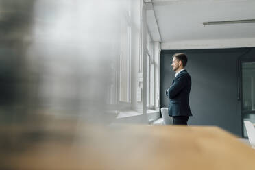 Porträt eines brünetten Geschäftsmannes, der im Büro aus dem Fenster schaut - GUSF03499