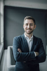 Portrait of smiling businessman with crossed arms in office - GUSF03503