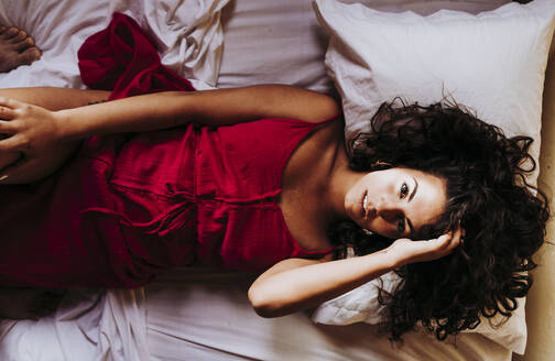 Porträt einer jungen Frau in rotem Kleid auf dem Bett liegend, Draufsicht - DAMF00392