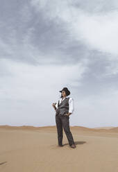 Modische junge Frau steht auf einer Düne und schaut in die Ferne, Wüste Merzouga, Marokko - DAMF00396