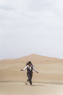 Modische junge Frau tanzt barfuß auf einer Sanddüne, Wüste Merzouga, Marokko - DAMF00397