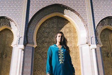 Young woman standing in front of traditional architure wearing Moroccan robe, Morocco - DAMF00401