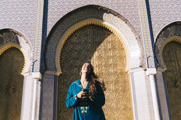 Young woman standing in front of traditional architure wearing Moroccan robe, Morocco - DAMF00402