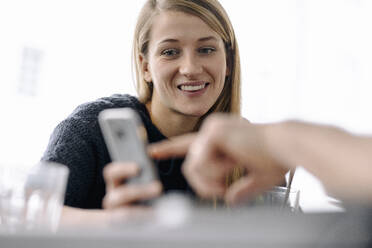 Portrait of smiling young woman and finger pointing on smartphone - GUSF03509