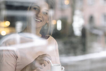 Porträt einer glücklichen jungen Frau hinter einer Fensterscheibe in einem Café - GUSF03531