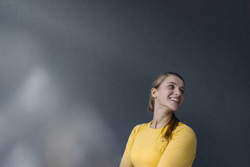 Porträt einer glücklichen jungen Frau an einer grauen Wand - GUSF03540