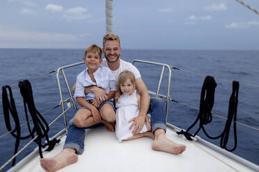 Father with his children sitting on boat deck during sailing trip - GMLF00094