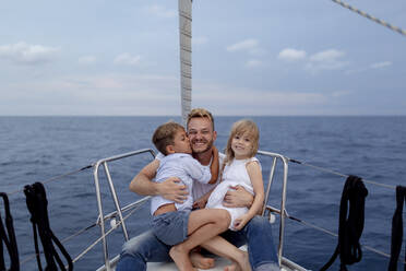 Father with his children sitting on boat deck during sailing trip - GMLF00097