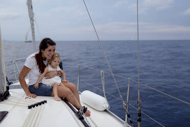 Mother and her daughter sitting on boat deck during sailing trip - GMLF00103