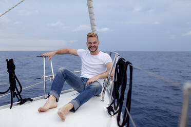 Smiling man sitting on boat deck during sailing trip - GMLF00110