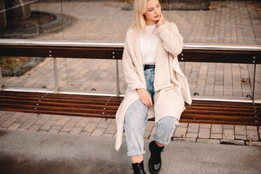 Thoughtful stylish young woman sitting on bus stop in city - CAVF79273
