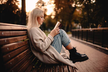 Teenager-Mädchen, das im Herbst auf einer Bank im Park sitzt und ein Buch liest - CAVF79281