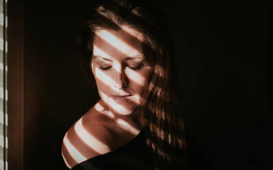 Portrait of woman beside a window with shadows across her face. - CAVF79329