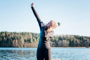 Woman putting a wetsuit on for cold water swimming at the beach - CAVF79394