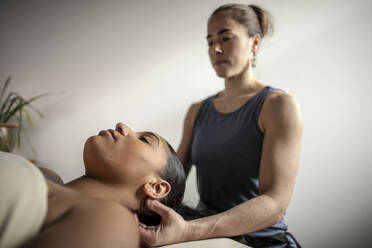 Female massage therapist works on neck of african american patient - CAVF79415