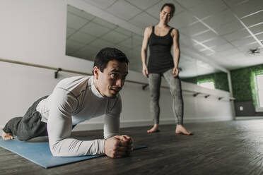 Mann macht Planke, während sein weiblicher Personal Trainer im Hintergrund trainiert - CAVF79439