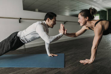Male and female friends high five while doing pushups at gym - CAVF79441