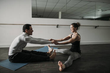 Lying on yoga mat young Woman holding muscular man on lifting legs