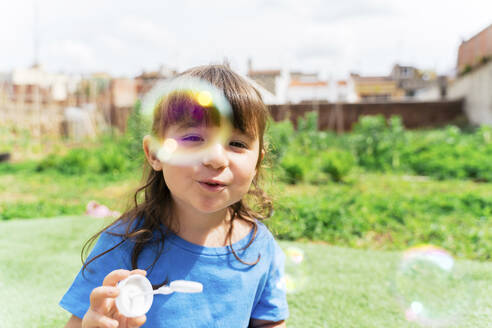 Portrait of happy little girl blowing soap bubbles in a park - GEMF03605