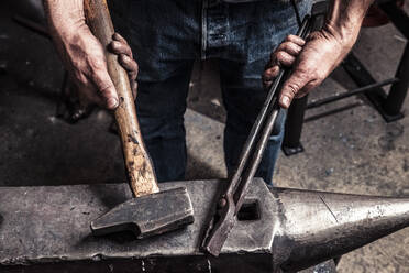 Knife maker holding pliers and hammer on anvil - WFF00366