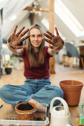 Young woman planting on wooden floor shwin her dirty hands - GUSF03557