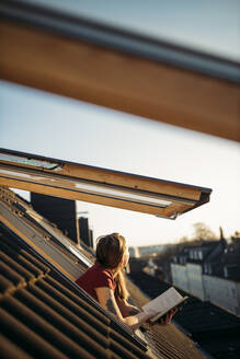 Junge Frau mit einem Buch am Fenster und Blick nach draußen - GUSF03564