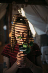 Junge Frau hält Zucchinipflanze zu Hause - GUSF03578
