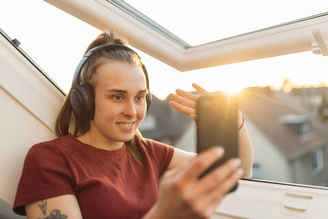 Junge Frau bei einem Video-Chat am Fenster im Gegenlicht, lizenzfreies Stockfoto