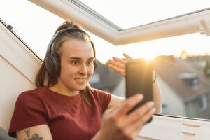 Junge Frau bei einem Video-Chat am Fenster im Gegenlicht - GUSF03588
