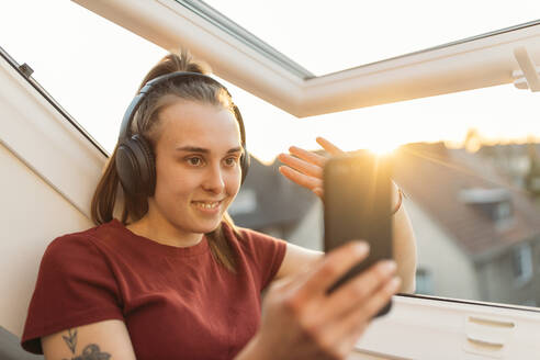 Young woman having a video chat at the window in backlight - GUSF03588