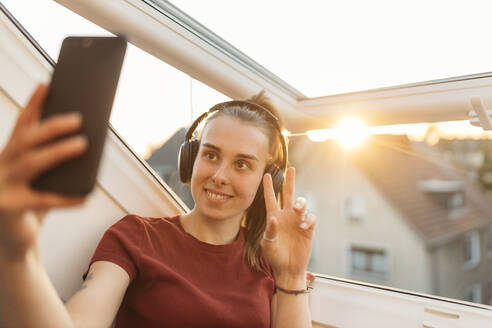 Junge Frau bei einem Video-Chat am Fenster im Gegenlicht - GUSF03589