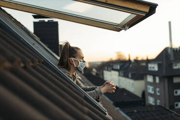 Junge Frau mit Maske schaut aus dem Fenster - GUSF03591