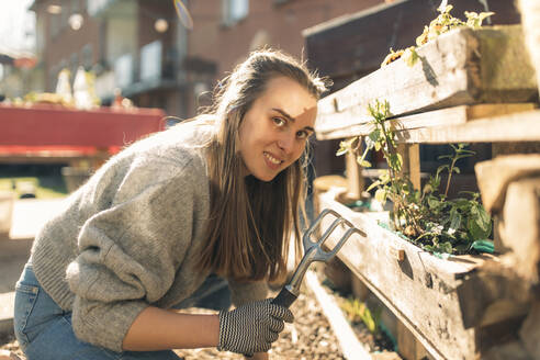 Portrait of young woman working in garden in sunshine - GUSF03602