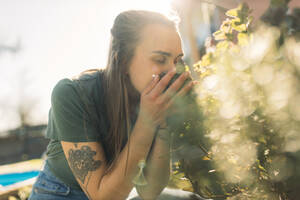 Junge Frau riecht an Kräutern im Garten - GUSF03615