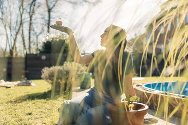 Young woman holding a seedling in garden in sunshine - GUSF03616