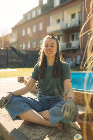 Young woman in garden balancing a flowerpot with seedling on her head stock photo