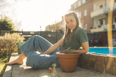 Junge Frau im Garten mit Setzling im Blumentopf - GUSF03619