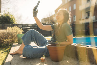 Junge Frau im Garten mit Setzling im Blumentopf macht ein Selfie - GUSF03621