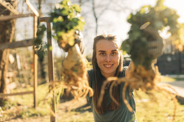 Proud young woman holding celeriac in garden - GUSF03636