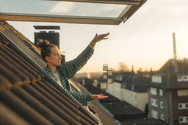 Junge Frau, die abends am Fenster ein Muster auf einer Schnur hält - GUSF03659