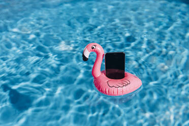 Smartphone on pink flamingo float in swimming pool - GUSF03682