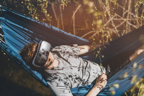 Junger Mann entspannt sich in der Hängematte, mit VR-Brille - GUSF03704