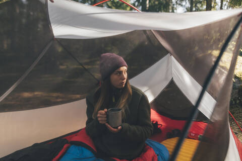 Junge Frau im Zelt im Wald, trinkt Tee, lizenzfreies Stockfoto