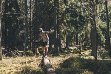 Young man balancing on tree trunk, looking through VR glasses - GUSF03708